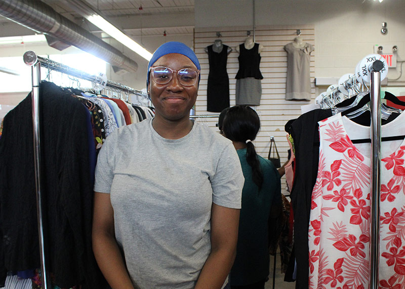 volunteer Friendly woman standing in between two clothing racks in a store